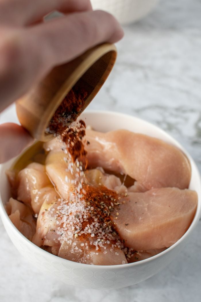 spices are shown being dumped on top of oiled chicken in a bowl